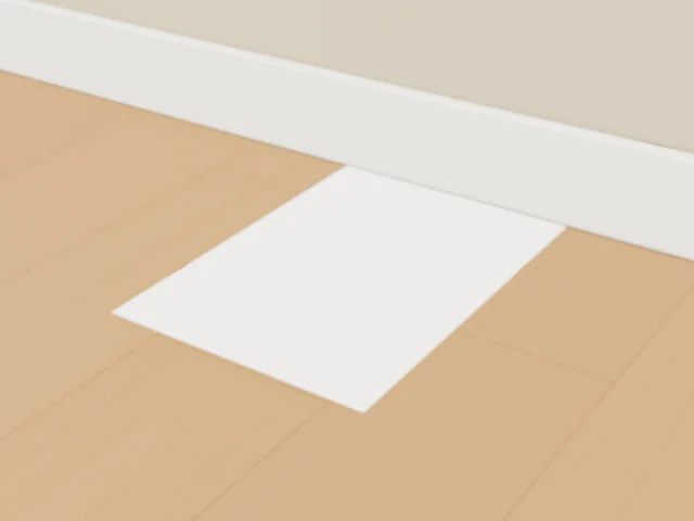 A sheet of paper on a wooden floor, its short edge pushed up against the skirting board.